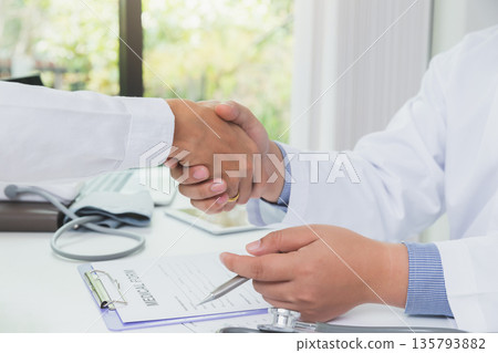 Doctor and patient shaking hands at office desk in hospital. Healthcare and medicine banner. Doctor shaking hands with patient after talking about medical examination results. 135793882