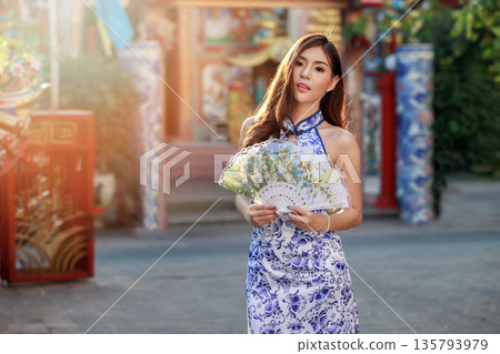Chinese woman in cheongsam dress holding fan at shrine. Concept to celebrate Chinese New Year. Chinese woman in cheongsam dress holding fan at shrine. Concept to celebrate Chinese New Year. 135793979