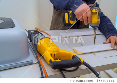 Carpenter drills into wood while using saw on work table in workshop 135794545