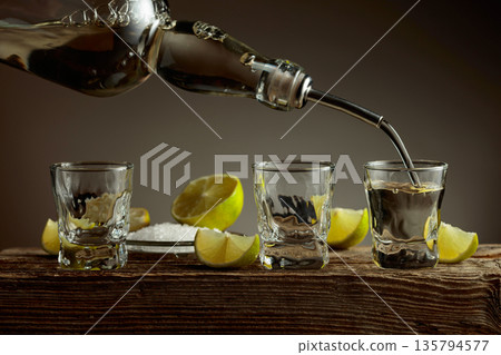 Tequila with salt and lime slices on a old wooden board. Tequila with salt and lime slices on a old wooden board. 135794577