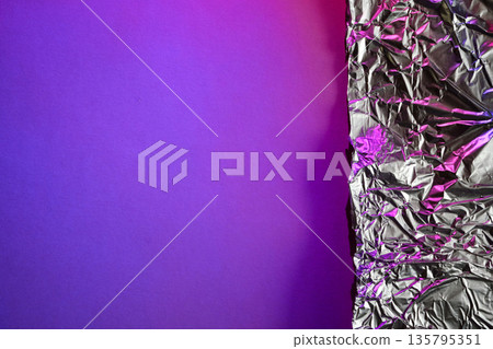 Crumpled metallic foil on vibrant purple background illuminated by neon pink light Crumpled metallic foil on vibrant purple background illuminated by neon pink light 135795351