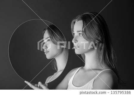Woman holding mirror reflecting profile portrait, self-reflection 135795386