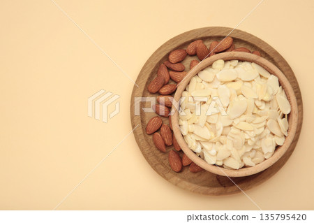 Fresh almond flakes and nuts in bowl on beige background Fresh almond flakes and nuts in bowl on beige background 135795420
