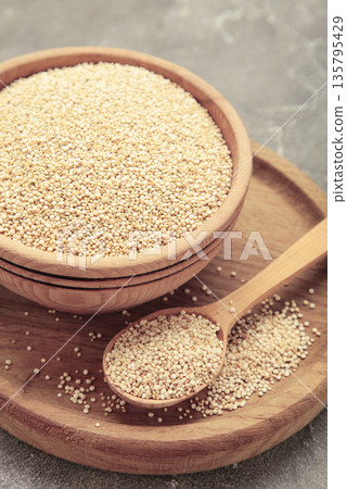 Organic white quinoa seeds in plate and spoon on grey background. Organic white quinoa seeds in plate and spoon on grey background. 135795429