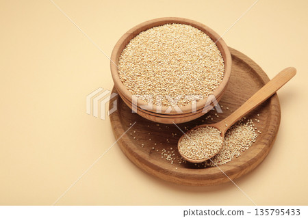 Organic white quinoa seeds in plate and spoon on beige background. Organic white quinoa seeds in plate and spoon on beige background. 135795433