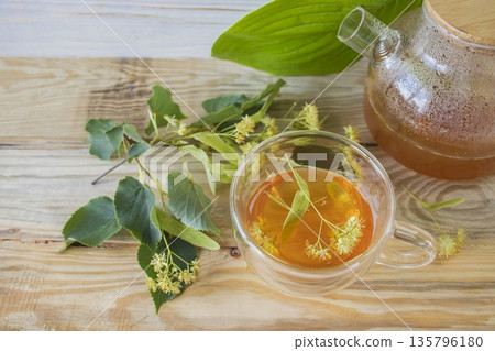 Linden tea in a glass cup with fresh linden flowers, on a wooden background. Medicinal herbal tea. 135796180