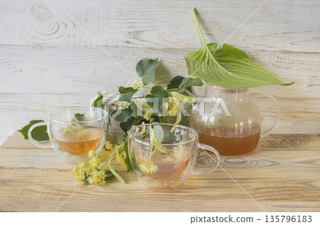 Linden tea in a glass cup with fresh linden flowers, on a wooden background. Medicinal herbal tea. 135796183