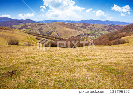 rural landscape with village in valley. outdoor adventures in countryside with rolling hills and snowy mountains in early spring. green environment sustainability and protection background rural landscape with village in valley. outdoor adventures in countryside with rolling hills and snowy mountains in early spring. green environment sustainability and protection background 135796192