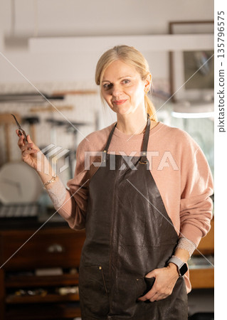 Woman jeweler working in artisan workshop holding tool Woman jeweler working in artisan workshop holding tool 135796575