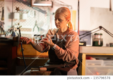 Woman artisan crafting glass art in workshop Woman artisan crafting glass art in workshop 135796578