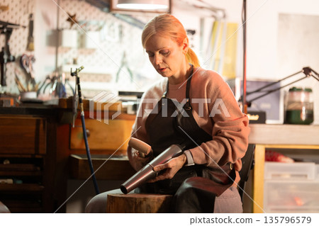 Woman forming metal vessel using hand tools in workshop 135796579