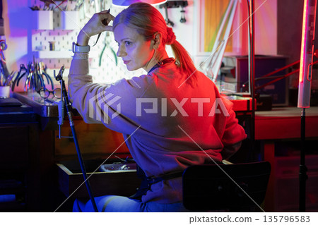 Woman working in optical workshop with colorful neon lights Woman working in optical workshop with colorful neon lights 135796583