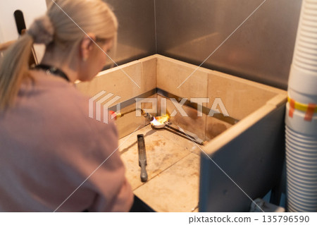 Woman goldsmith melting metal using torch in workshop Woman goldsmith melting metal using torch in workshop 135796590