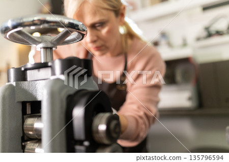 Woman crafting jewelry using a metal rolling mill machine Woman crafting jewelry using a metal rolling mill machine 135796594