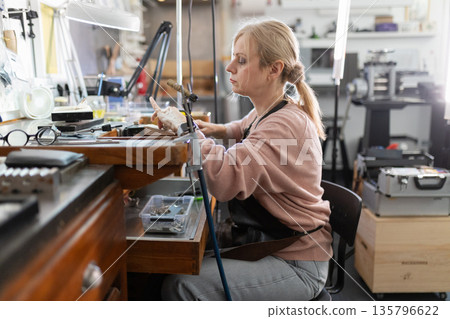 Woman jeweler focusing on intricate craftsmanship in workshop Woman jeweler focusing on intricate craftsmanship in workshop 135796622