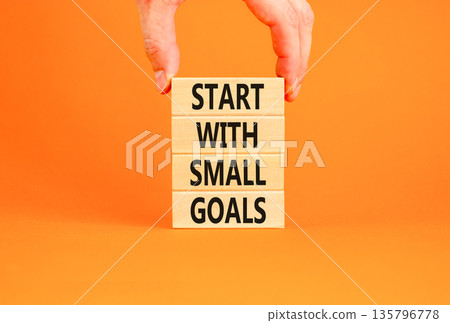 Start with small goals symbol. Concept words phrase Start with small goals on beautiful wooden blocks. Beautiful orange background Businessman's hand Business Start with small goals concept Copy space 135796778