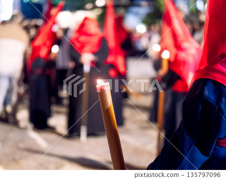 Close up of a lit candle held by a nazareno in procession 135797096