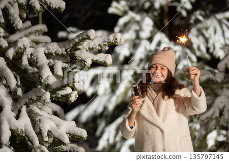 Woman celebrating new year's eve with champagne and sparkler in snowy forest Woman celebrating new year's eve with champagne and sparkler in snowy forest 135797145