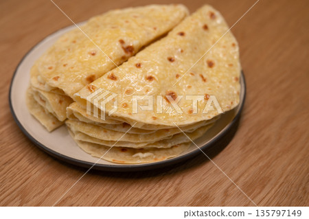 Stack of golden flatbreads resting on a ceramic plate 135797149