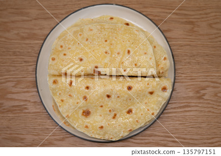 Traditional flatbread resting on a ceramic plate on a wooden table 135797151