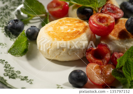 Cheesecakes with cherries and blueberries garnished with fresh mint leaves on white plate 135797152