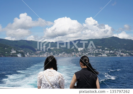 兩名年輕女子從船上眺望熱海市和大海。 兩名年輕女子從船上眺望熱海市和大海。 135797262