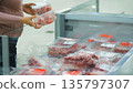 Woman choosing packaged meat in a supermarket freezer, examining freshness and label details, shopping and food consumer lifestyle 135797307