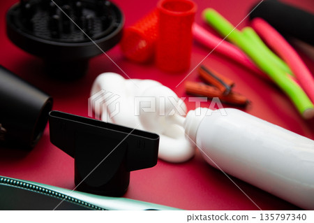 Close-up side view on a pink background, hairdryer with attachments, stylers and curling irons for straightening and creating curls, foam for volume and long-lasting, curlers in different shapes and Close-up side view on a pink background, hairdryer with attachments, stylers and curling irons for straightening and creating curls, foam for volume and long-lasting, curlers in different shapes and 135797340