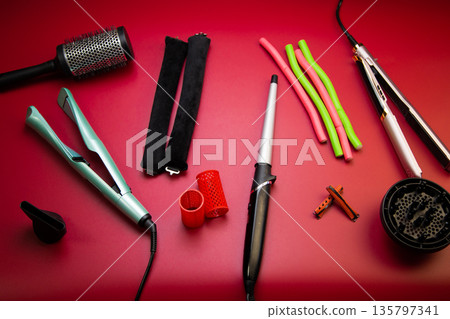 A fold on a pink background, stylers and curling irons for straightening and creating curls, curlers of different shapes and sizes, a round comb for volume. The concept of hair care, hairstyle A fold on a pink background, stylers and curling irons for straightening and creating curls, curlers of different shapes and sizes, a round comb for volume. The concept of hair care, hairstyle 135797341