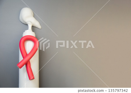 On the side, on a gray background, there is a bottle of foam for long-term hair styling, white foam poured out of it, on it lies a curved pink curler with space for text. The concept of styling 135797342