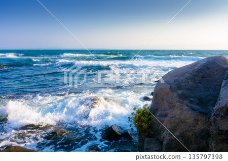 rocks at the black sea shore in summer. waves crashing coast of bulgaria on a sunny morning. cloudless blue sky. travel background at the seaside 135797398