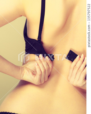 Woman dressing up her bra rear view Woman dressing up her bra rear view 135797522