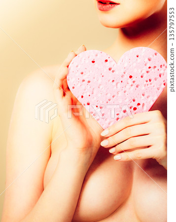 Naked woman holding pink heart sponge in hands. 135797553