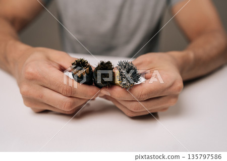 Person holding three steam cleaner brushes in close-up, showing new, partially worn, and heavily worn heads to illustrate replacement, maintenance, and cleaning effectiveness. 135797586