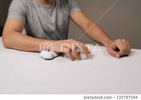 Close-up cropped shot of person using comfortable ergonomic wrist rest and computer mouse on white desk, focusing on wrist support, body posture, and injury prevention in a modern workplace setting. Close-up cropped shot of person using comfortable ergonomic wrist rest and computer mouse on white desk, focusing on wrist support, body posture, and injury prevention in a modern workplace setting. 135797594