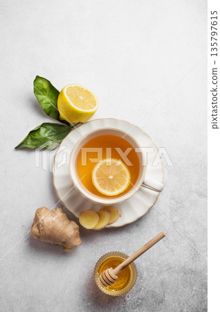 A cup of hot tea with fresh lemon and ginger on a light textured background with honey 135797615