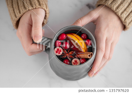A woman in a beige sweater holds a mug of non-alcoholic mulled wine or a spicy hot drink A woman in a beige sweater holds a mug of non-alcoholic mulled wine or a spicy hot drink 135797620
