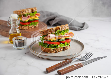 Sandwich with ham, cheese, lettuce, tomatoes, cucumbers and seeded bread on a plate Sandwich with ham, cheese, lettuce, tomatoes, cucumbers and seeded bread on a plate 135797624