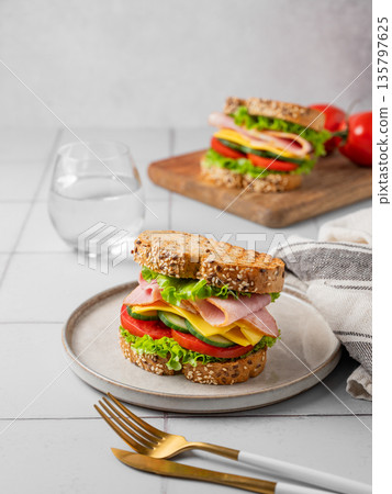Sandwich or toast with ham, cheese, lettuce and vegetables on a plate on a gray tile Sandwich or toast with ham, cheese, lettuce and vegetables on a plate on a gray tile 135797625