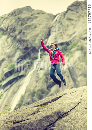 Happy woman jumping on rock in mountains Happy woman jumping on rock in mountains 135797716