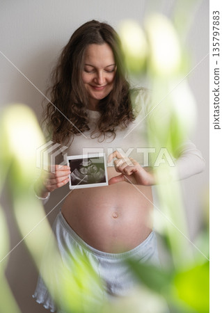Pregnant woman showing ultrasound scan with flowers in foreground Pregnant woman showing ultrasound scan with flowers in foreground 135797883