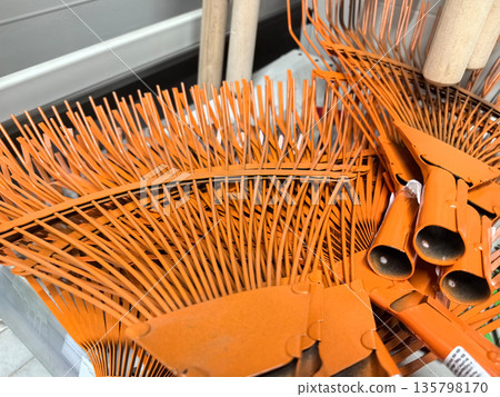 Bright orange rakes piled together in a garden supply area during the afternoon 135798170