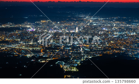 Wide aerial view of a densely built capital illuminated after sunset with streets, neighborhoods and mountain silhouettes in sunset sky, Tirana, Albania Wide aerial view of a densely built capital illuminated after sunset with streets, neighborhoods and mountain silhouettes in sunset sky, Tirana, Albania 135798660