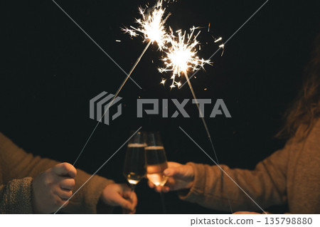 Friends celebrating with sparklers and champagne glasses at night. Festive atmosphere, New Year 2026 and holiday celebration, friendship, joy, party. 135798880