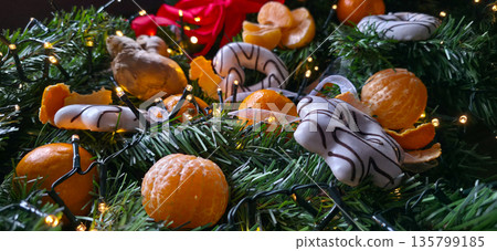 Tangerines, gingerbread, and a string of lights on fir branches. decorations and ornaments for the New Year. the festive atmosphere of Christmas and New Year. High quality photo Tangerines, gingerbread, and a string of lights on fir branches. decorations and ornaments for the New Year. the festive atmosphere of Christmas and New Year. High quality photo 135799185