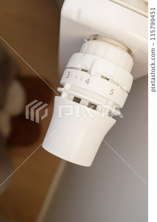 Woman in warm home winter sleepers adjusting temperature on radiator heating thermostat to middle position. Comfort and warmth at home in cold season, using smart home devices for economy. 135799451