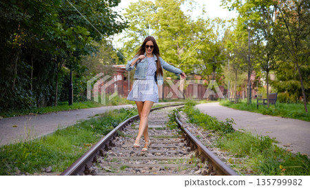 Confident young woman walking on tram tracks in summer park Confident young woman walking on tram tracks in summer park 135799982