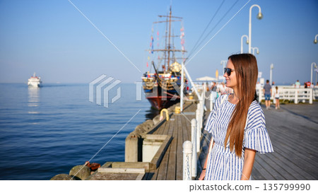 Young woman standing on pier and looking at sea on sunny day Young woman standing on pier and looking at sea on sunny day 135799990