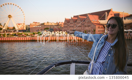 Woman on boat with Gdansk waterfront skyline and ferris wheel at sunset 135800045