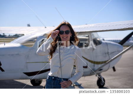 Smiling woman in sunglasses near light aircraft on sunny day 135800103